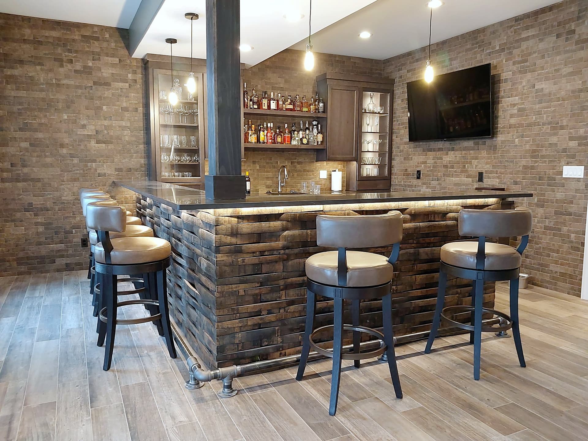 A finished basement bar with a brick wall and barrel-stave front