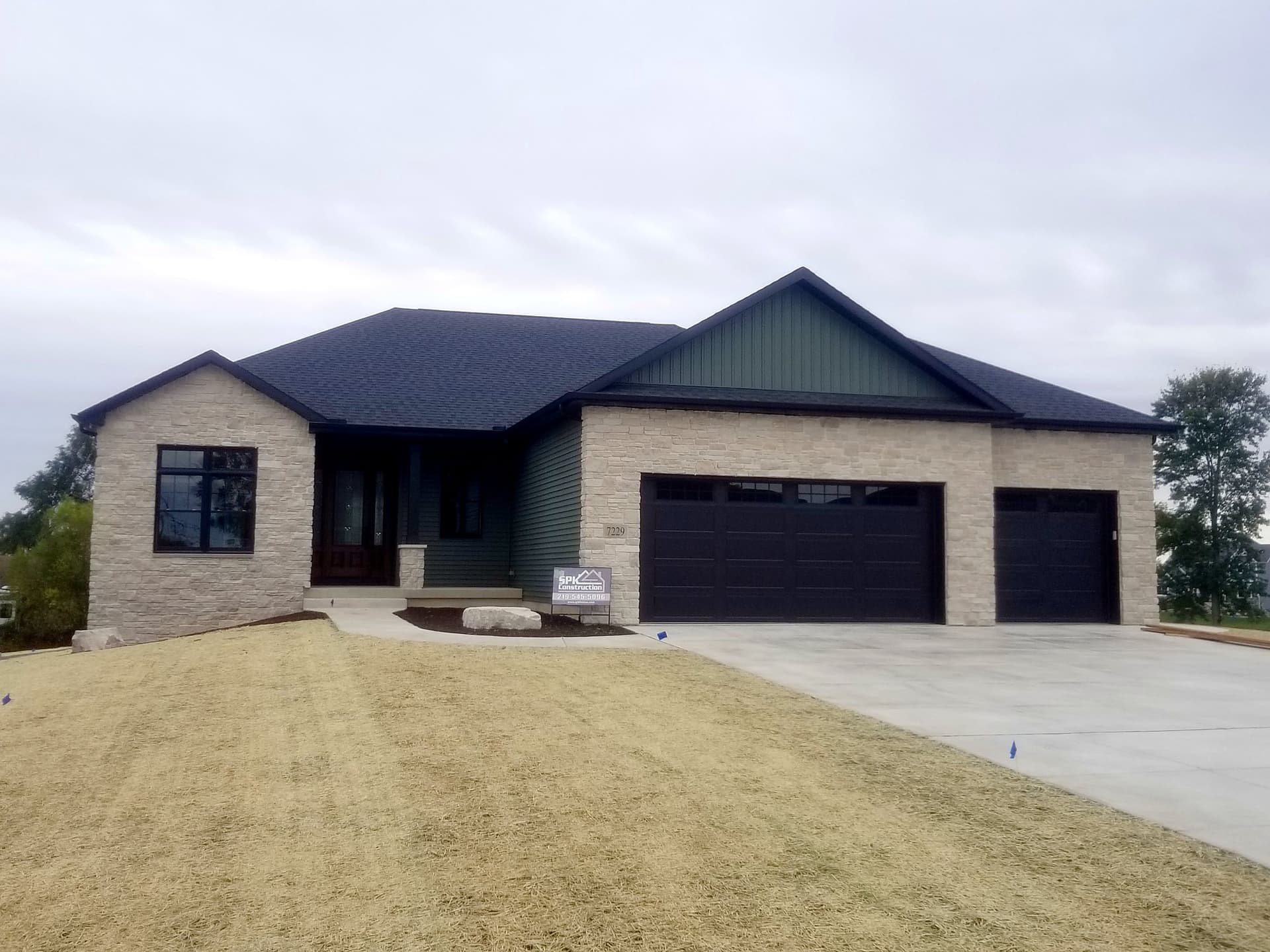 Stone and green-sided custom ranch with a three-car garage
