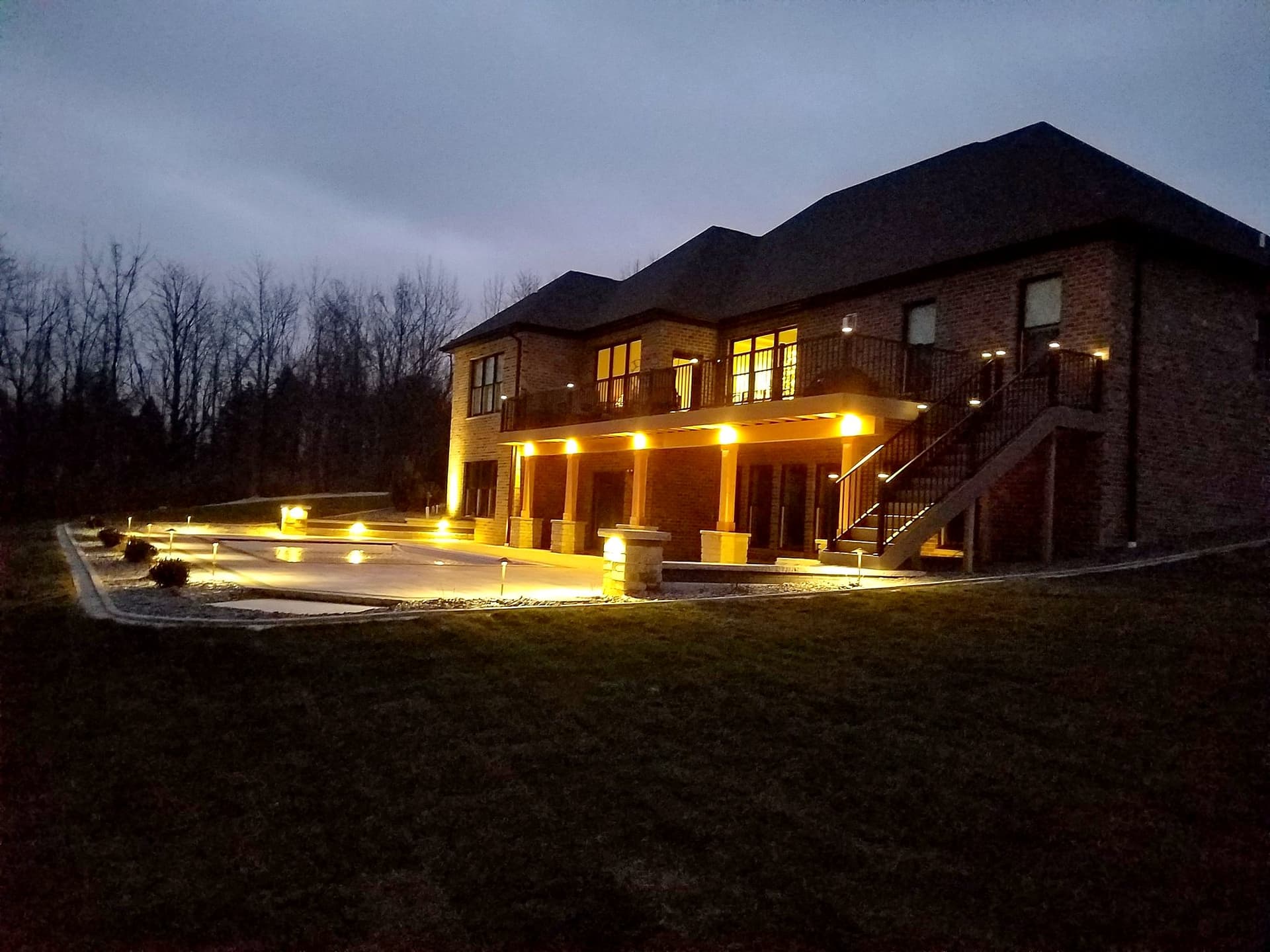 Brick custom home with a lit deck and patio at dusk